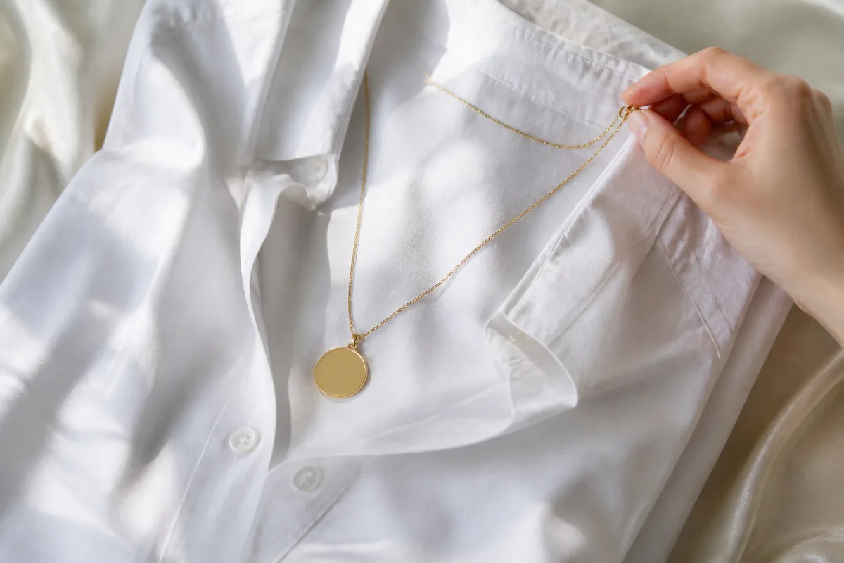 Chaine fine doree a pendentif medaille posee sur une chemise blanche pliee
